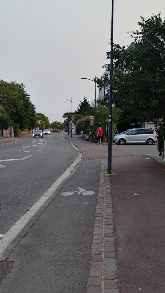 Une piste cyclable sur le trottoir. Elle s'arrête sur 5 m au niveau du parking du supermarché — je perds la priorité. Deux mètres plus loin, il y a un arrêt de bus : il faut ralentir pour ne pas surprendre les usagers assis sur le banc de l'abri de bus. Quinze mètres plus loin, il y a un rond-point ; étant sur le trottoir, je n'ai plus la priorité. Je dois m'arrêter au passage piéton pour aller tout droit, contrairement aux voitures qui peuvent s'élancer sur le rond-point. Entre la sortie du parking, l'arrêt de bus, les piétons et les bouts de verre récurrents, cette piste cyclable est un véritable enfer. On avance deux fois moins vite que si l'on était sur la route avec les voitures.